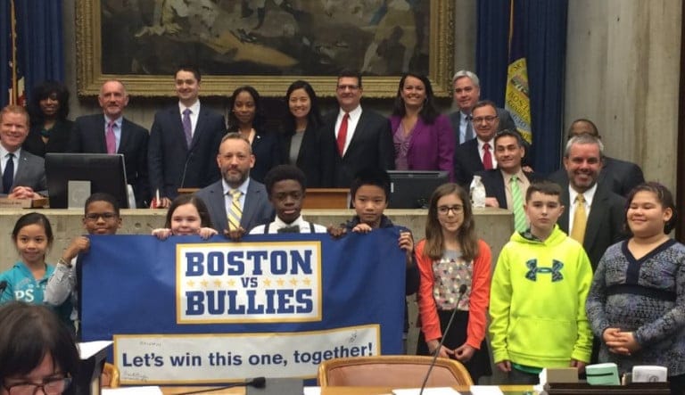 Boston City Councilors standing with students in front of a Boston vs. Bullies podium