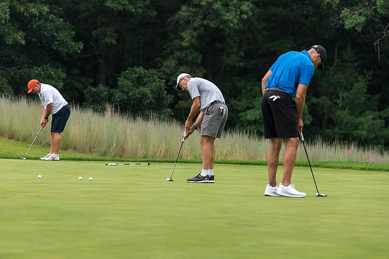 Three golfers on the putting green lining up their shots.