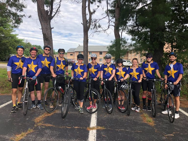 Group of 11 people with bicycles in front of them lined up for a photo before a race.