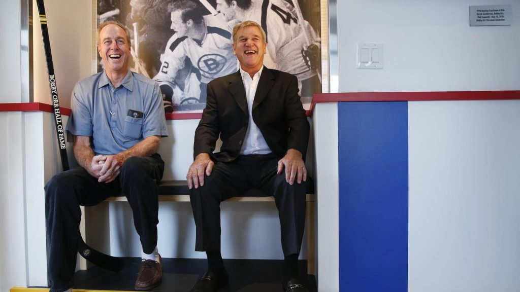 two men sitting on a bench in a hockey penalty box