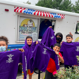 Students wearing masks and holding up purple hoodies.,